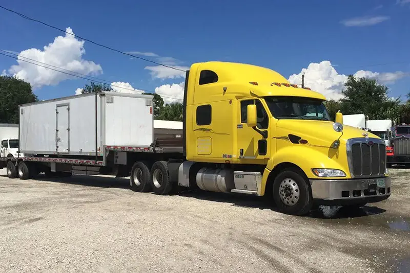 Tractor hauling a flatbed trailer loaded with a used van body on the DeBary lot